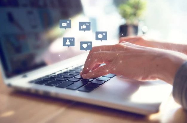 Hands typing on a laptop with social media icons floating above the screen